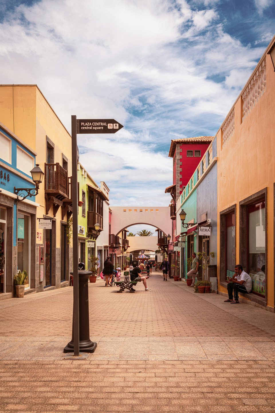 Pedestrians walk along a shopping street lined with pastel buildings.